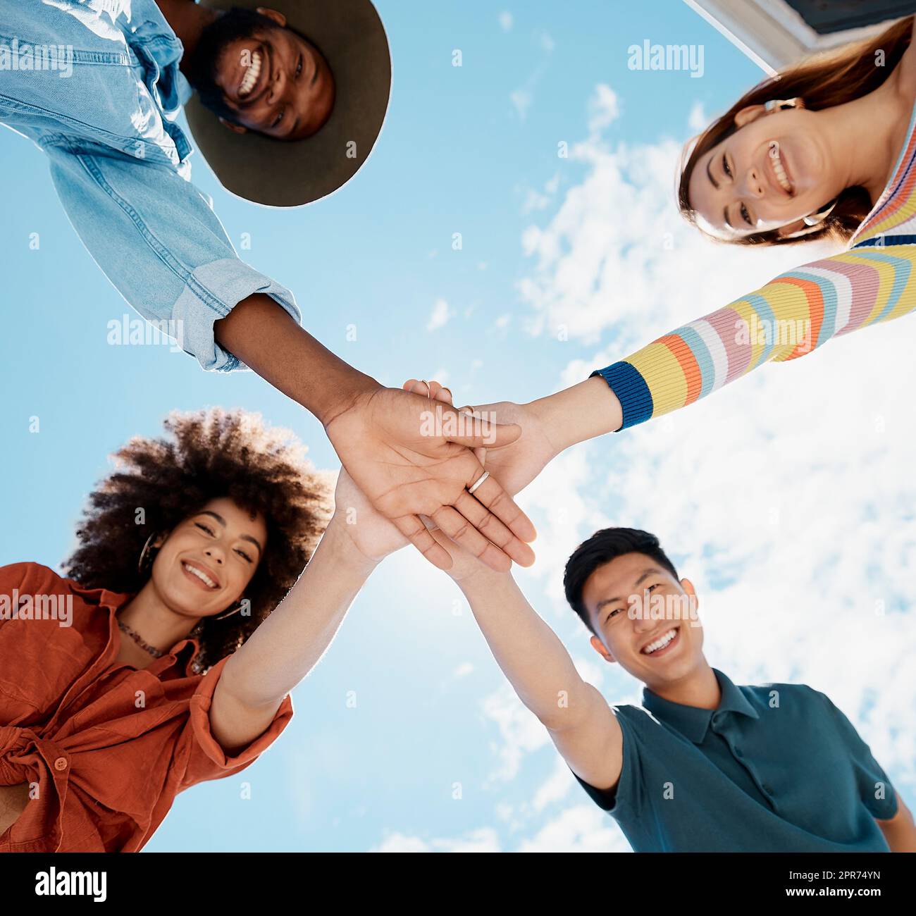 Low angle view of diverse group of people standing huddled together with hands piled in the middle. African American woman with an afro. Millennial social clique stacking hands in unity and support Stock Photo