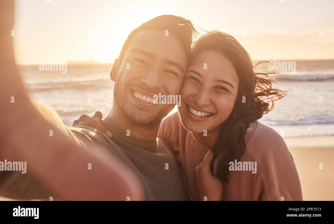 Portrait of a young diverse biracial couple taking a selfie at the beach and having fun outside. Portrait of a young diverse biracial couple taking a selfie at the beach and having fun outside. Stock Photo