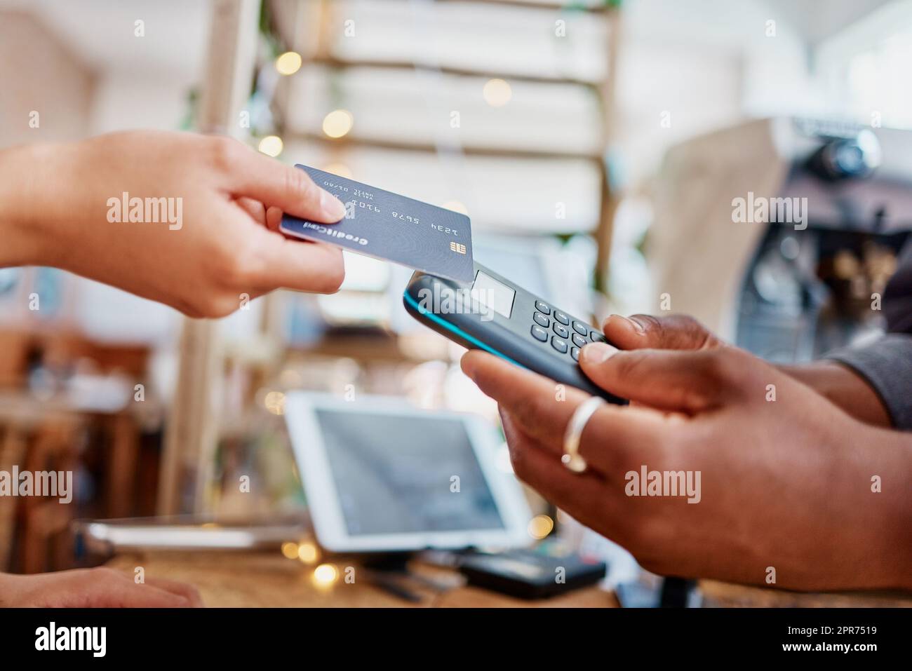 Closeup of unknown mixed race customer using a wireless credit card machine to pay for her coffee. African american barista assisting a woman in a cafe. Contactless paying system during covid pandemic Stock Photo