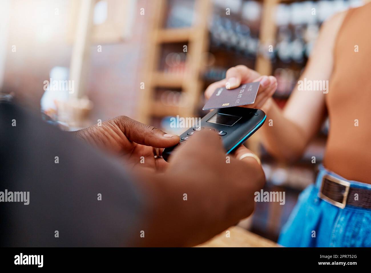 Closeup of unknown mixed race customer using a wireless credit card machine to pay for her coffee. African american barista assisting a woman in a cafe. Contactless paying system during covid pandemic Stock Photo