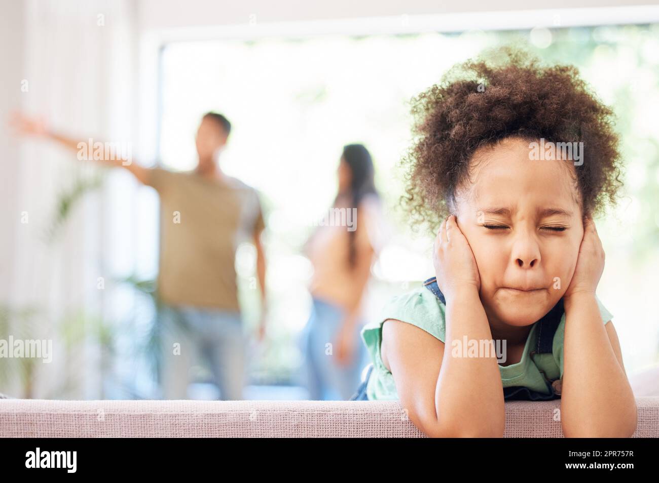Ive gotten used to blocking them out. Shot of a little girl covering her ears while her parents argue in the background. Stock Photo