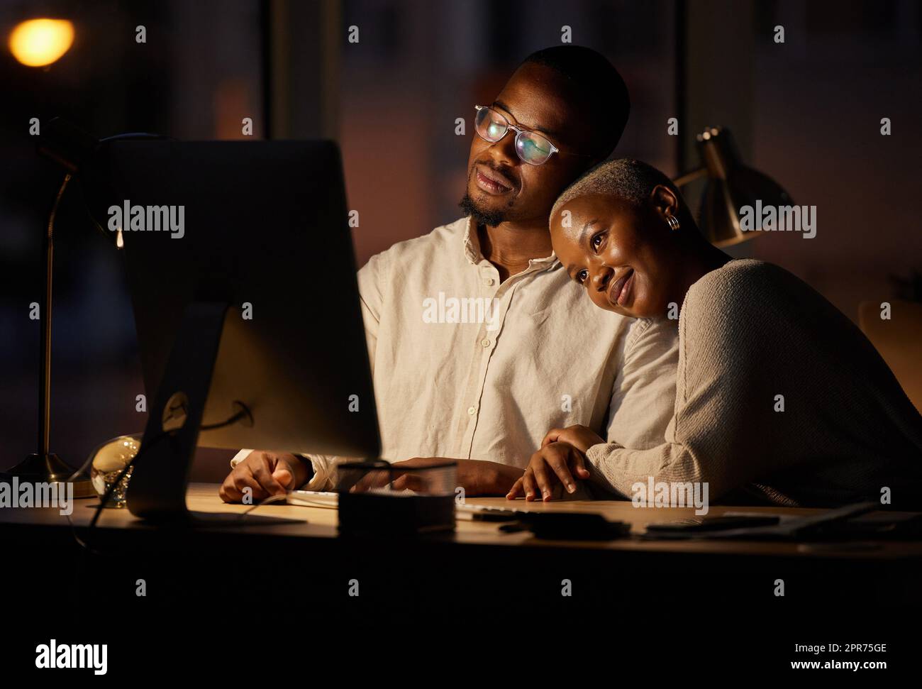 The romance is brewing between them. Shot of two affectionate businesspeople working together on a computer in an office at night. Stock Photo