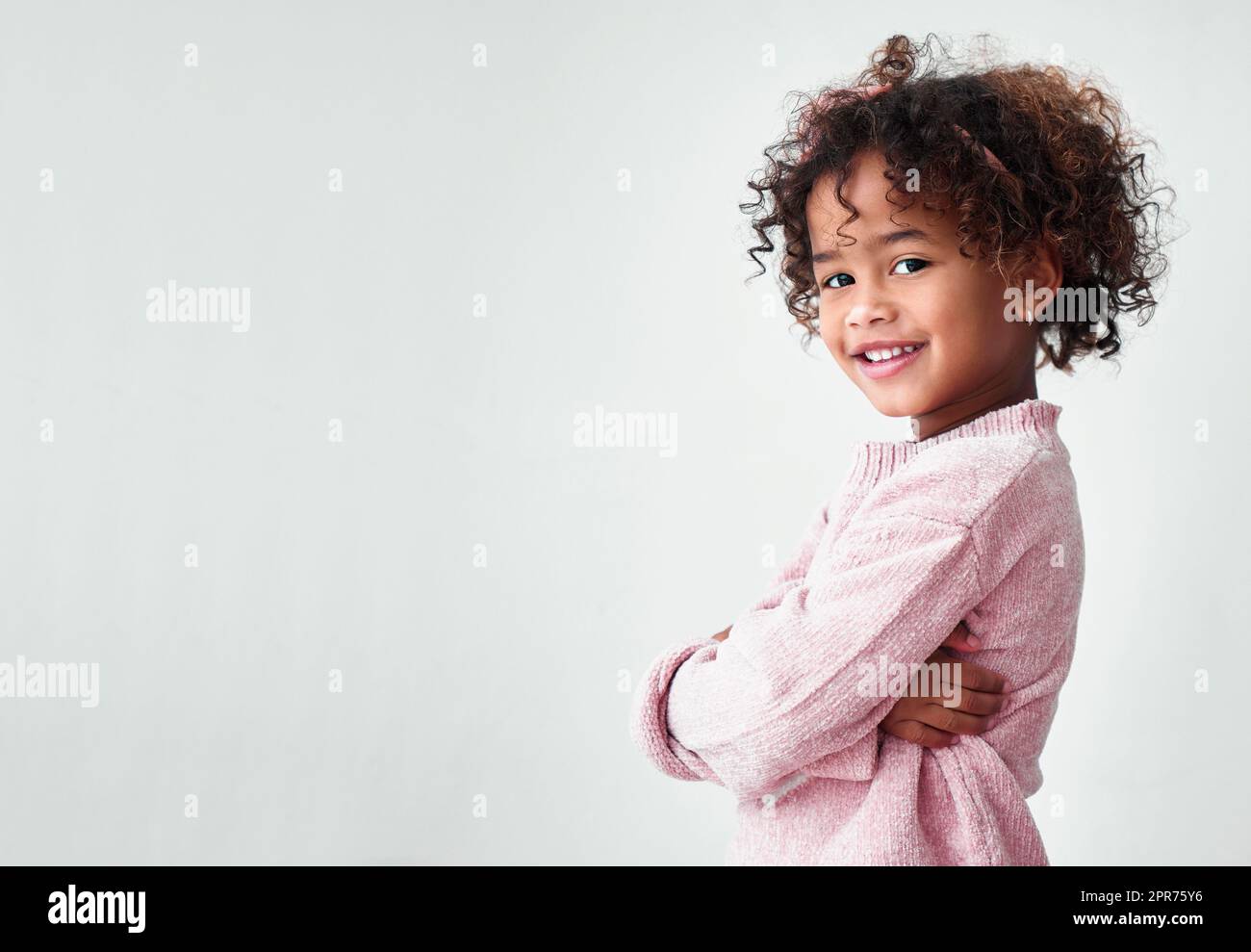 Shes laughter and joy. Shot of a little girl standing with crossed arms against a grey background. Stock Photo