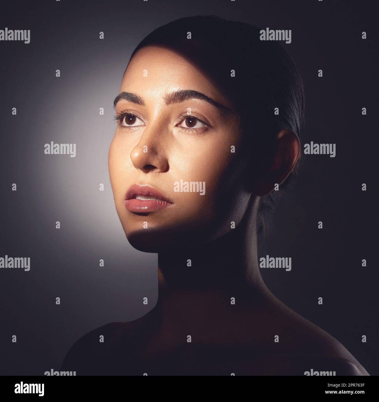A major component of healthy skin is a natural glow. Studio shot of a beautiful young woman posing with light beam against her face. Stock Photo