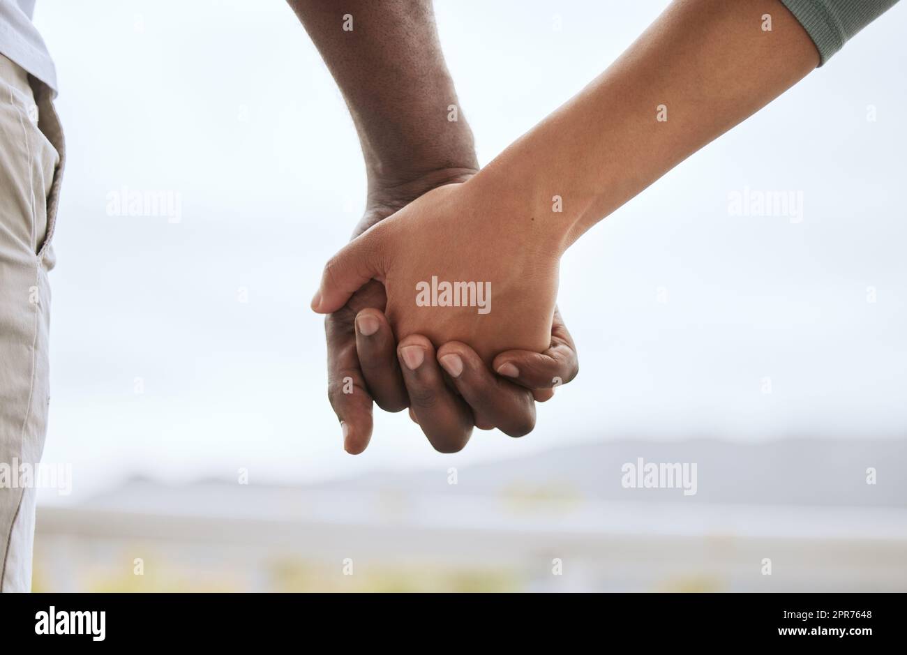Closeup of biracial couple interlocking fingers and holding hands while