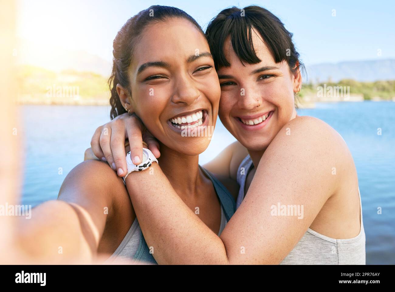 Portrait of two smiling friends taking selfies together for social media on a lake over summer break. Smiling happy women bonding and hugging outside in nature. Embracing and having fun on weekend Stock Photo