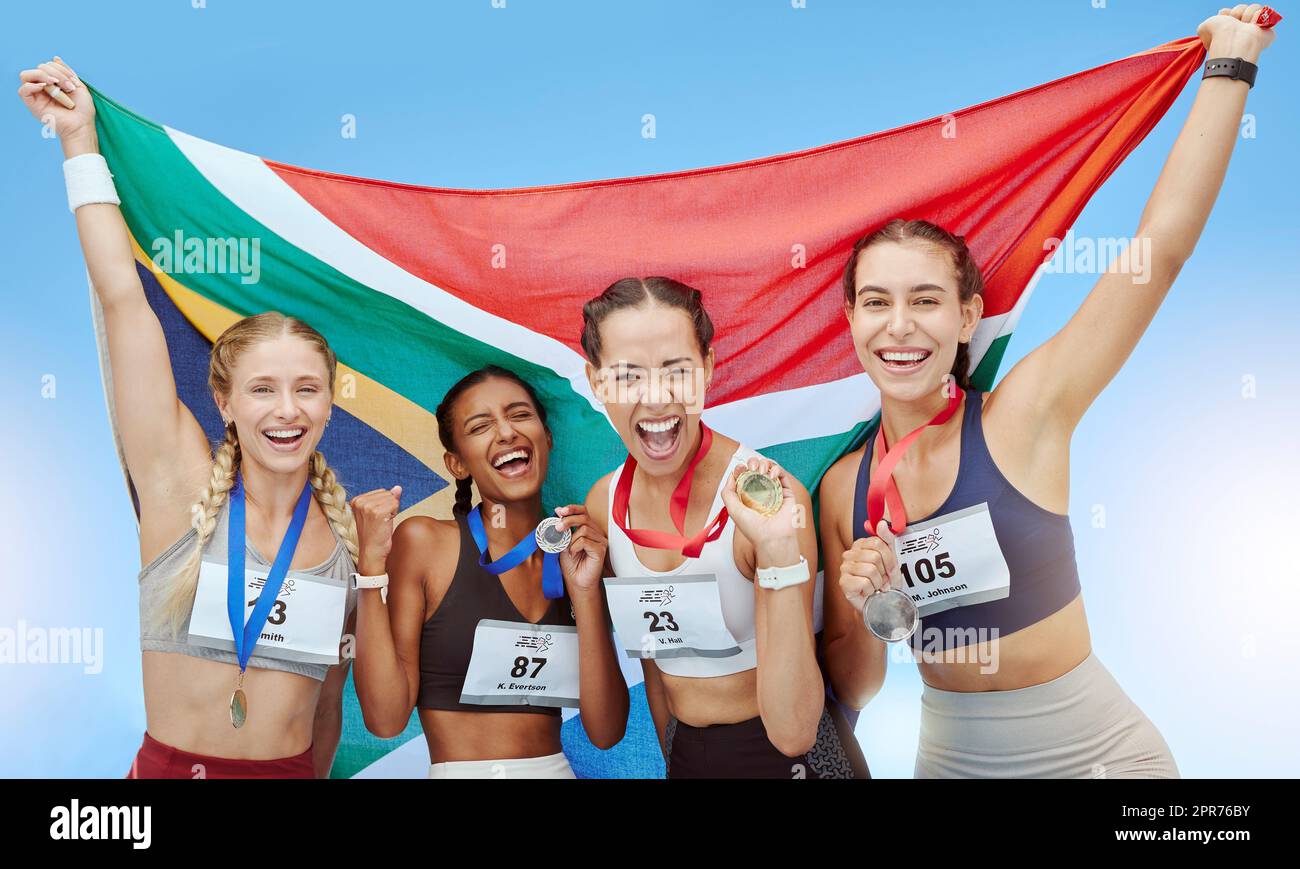 Portrait diverse group of female olympic athletes holding winners medals and African flag. Happy and proud champions of South Africa. Winning a medal for your country is an amazing achievement Stock Photo