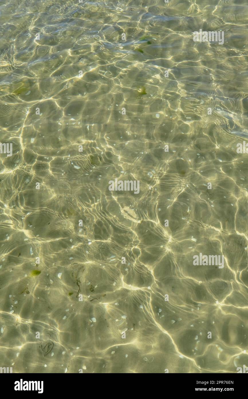 Above view of sunlight reflecting off water at beach with copy space. Shallow waves and calm ripples on coastline on sunny day outside. Clear liquid refracting sun rays against summer background Stock Photo