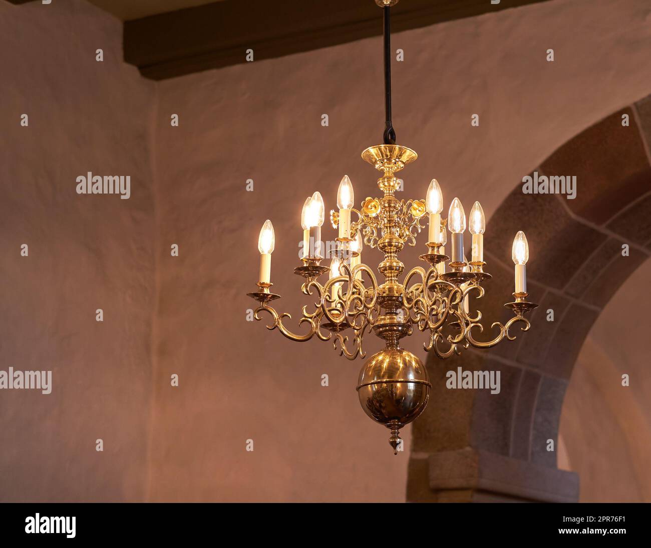 Old fashioned brass chandelier with candle light bulbs hanging from roof or ceiling in a historic building and vintage room. Shiny ornamental, medieval, ancient and antique light fixture in a mansion Stock Photo