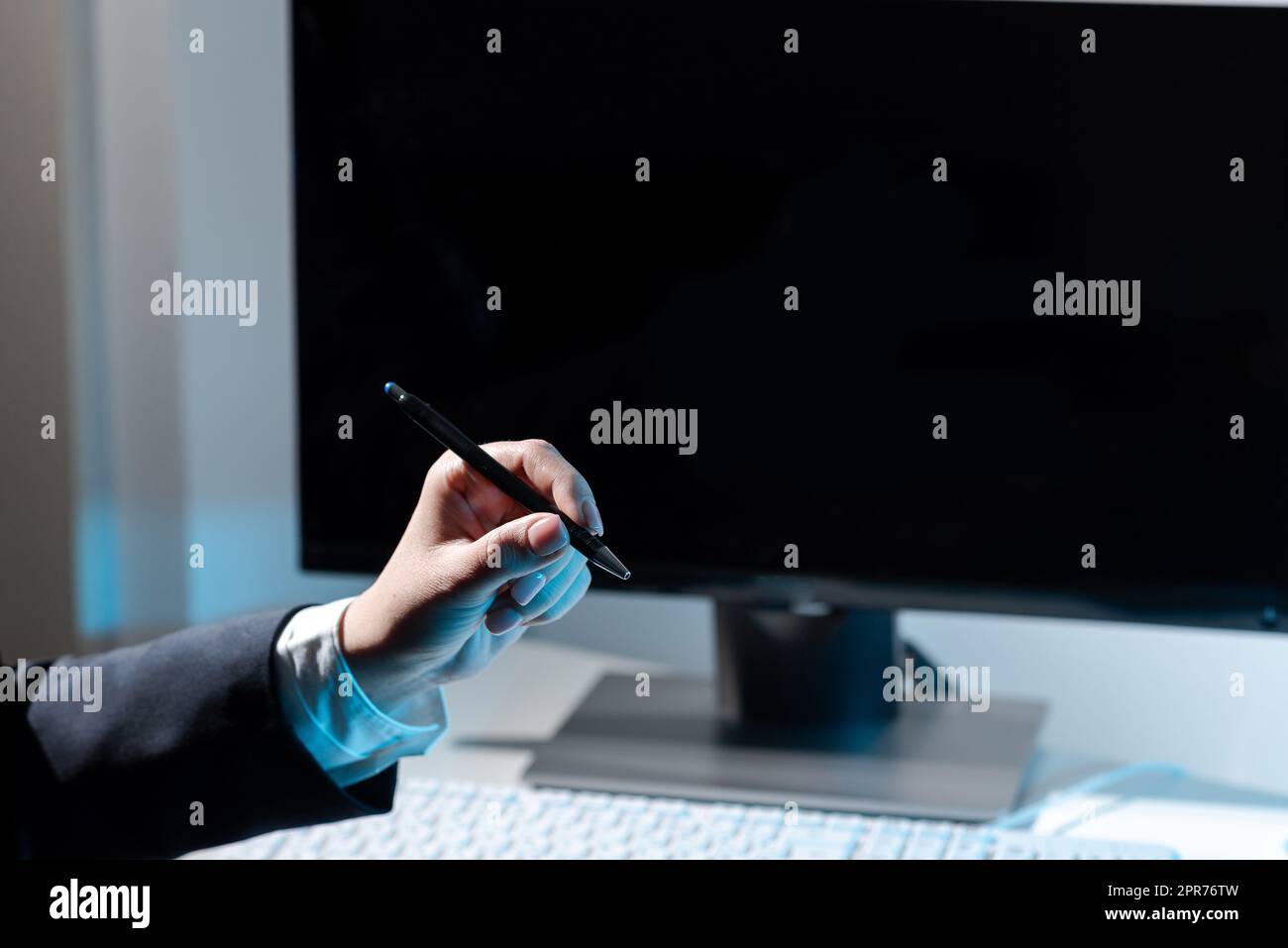 Businesswoman Holding Pen And Pointing On Important Messages On Table With Computer And Keyboard. Woman Presenting Crutial Information With One Hand. Stock Photo