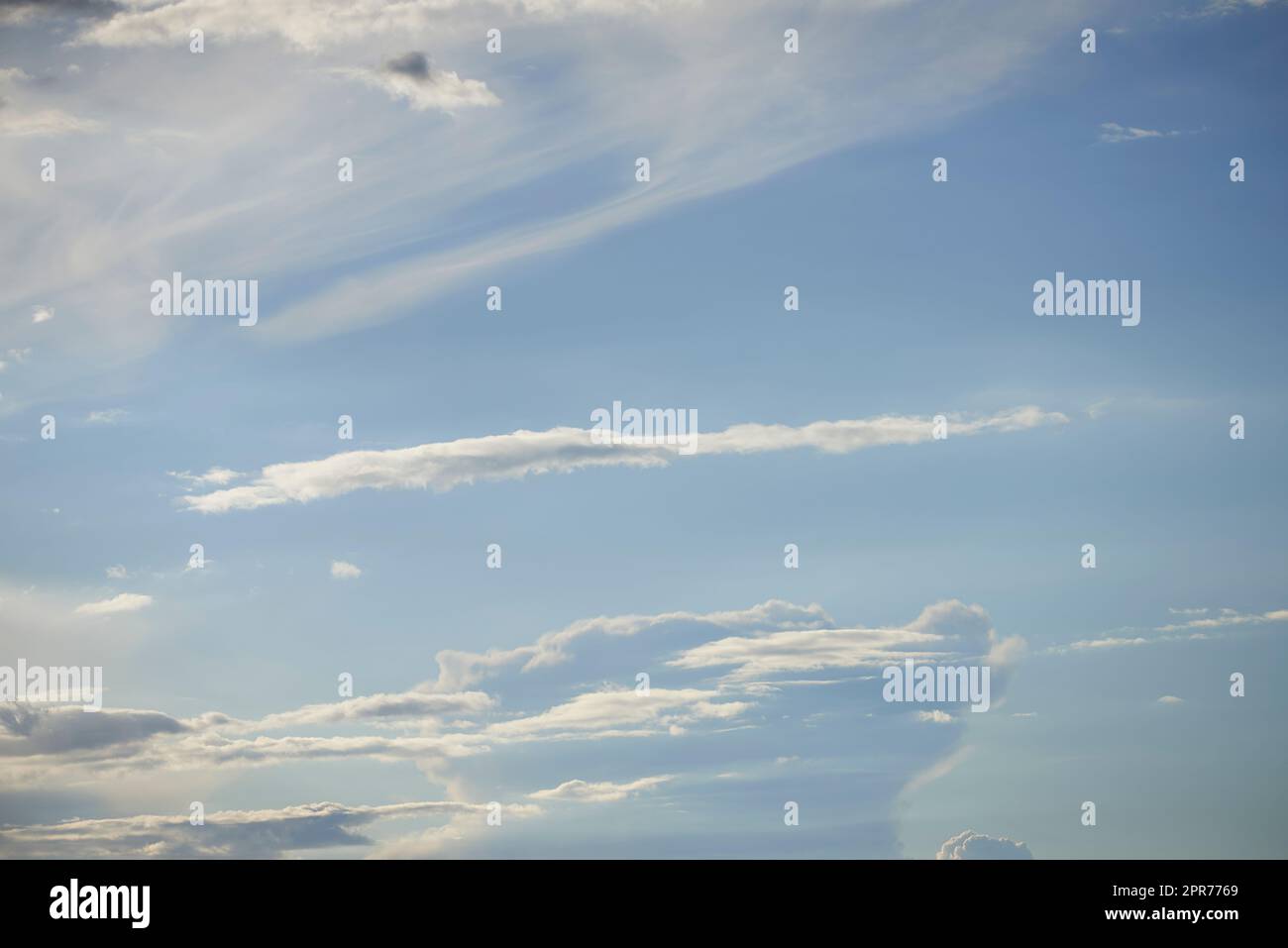 Light clouds in a blue sky with copy space background. A beautiful clear summer sky with sunshine and a white soft textured cloudscape in nature. Calming skies clearing up on a sunny day Stock Photo