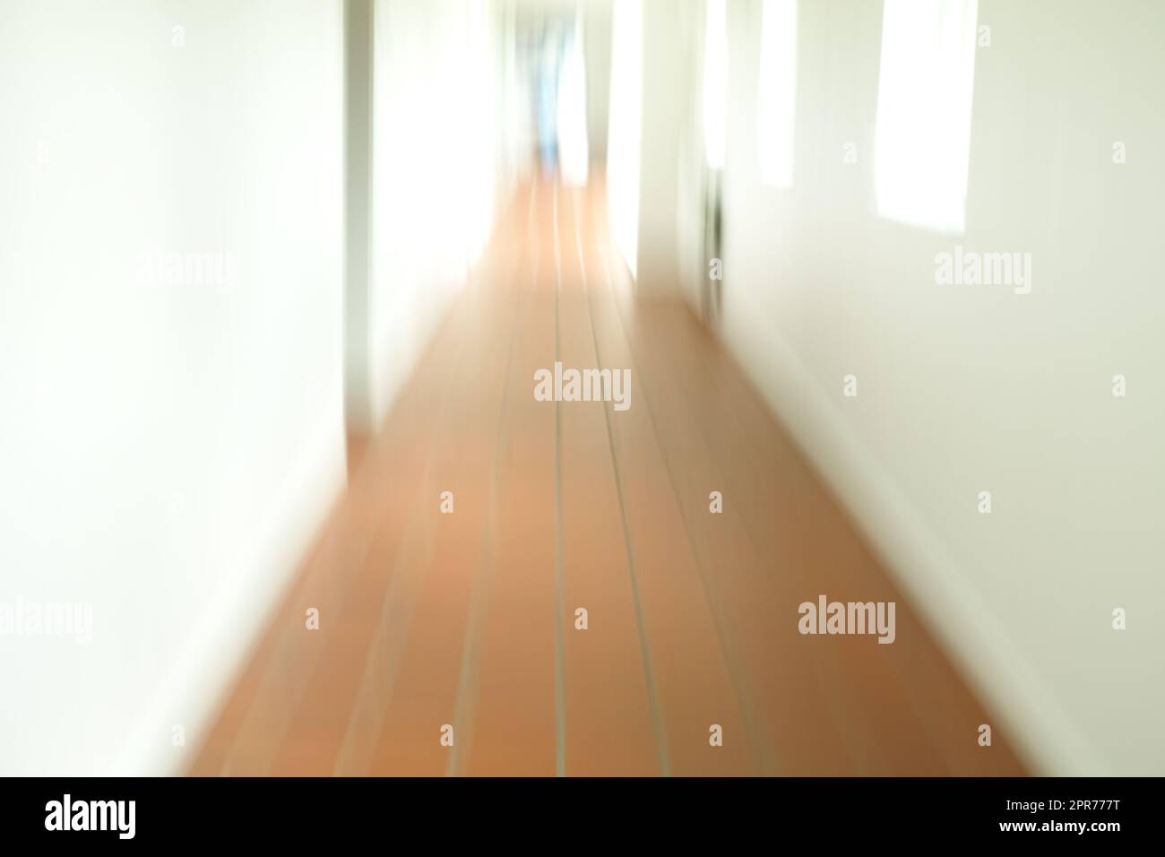 A blurry tiled hallway with white walls and sun shining through the open windows. An empty hospital, clinic or school corridor Stock Photo