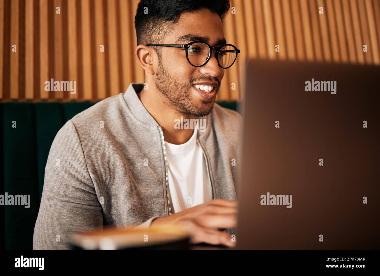 .. Handsome indian man with glasses sitting alone and using laptop in cafe. Man using wifi to browse the internet or doing freelance work in a cafe. Male student doing research on internet. Stock Photo