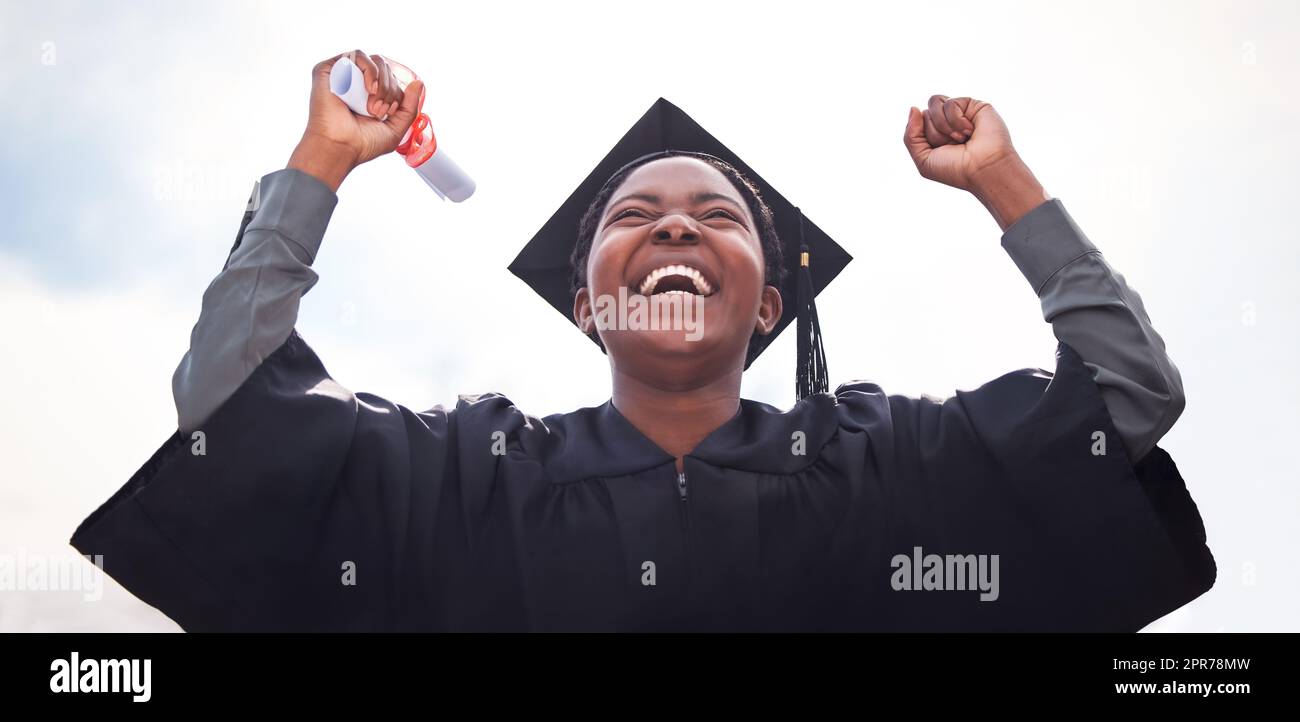 I achieved my hearts desires. Low angle shot of a young woman cheering on graduation day. Stock Photo