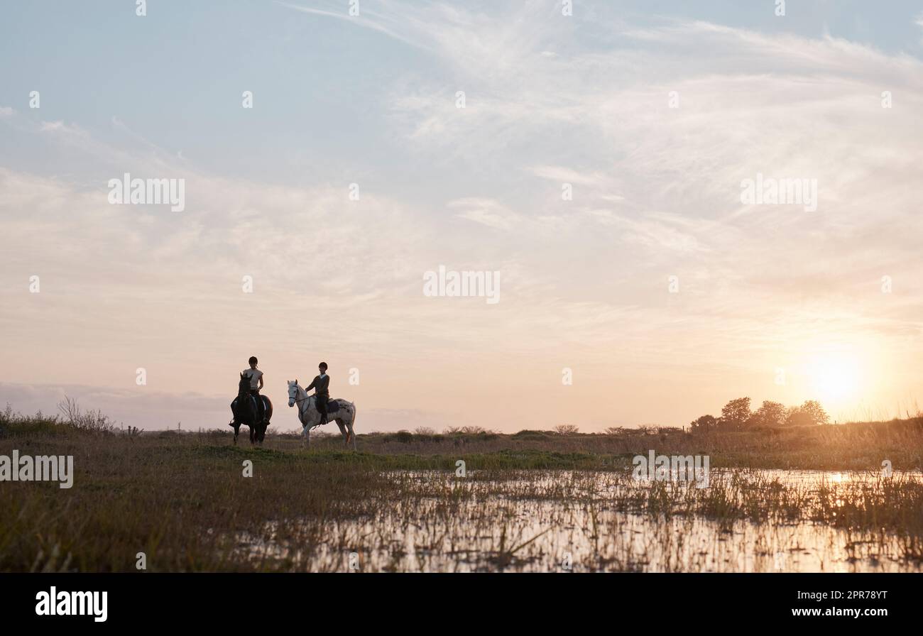 Feel the air, smell the foliage and explore natures beauty. Shot of two young women out horseback riding together. Stock Photo