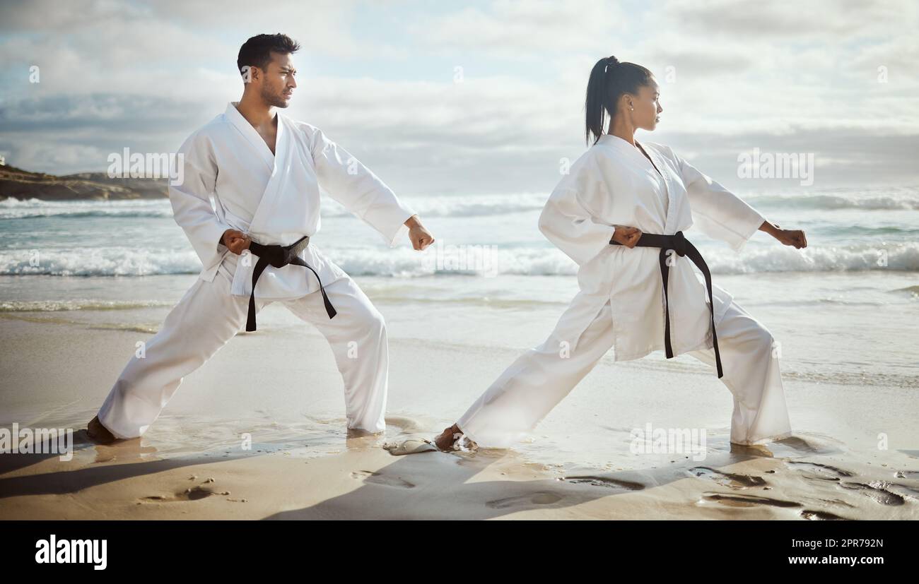You lead, Ill follow. Full length shot of two young martial artists practicing karate on the beach. Stock Photo