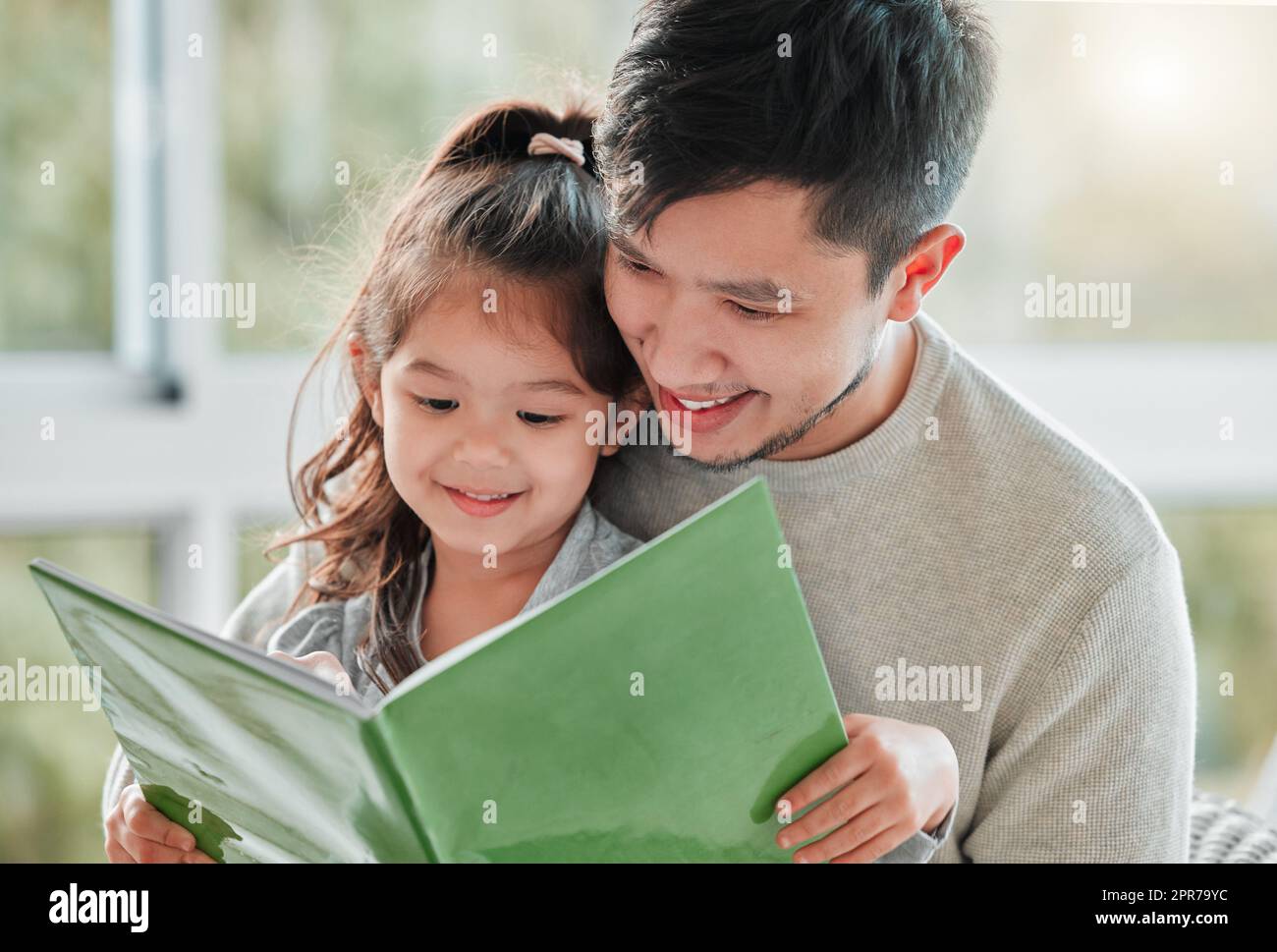 Theres always time for a story. of a little girl sitting on her fathers lap with a book. Stock Photo