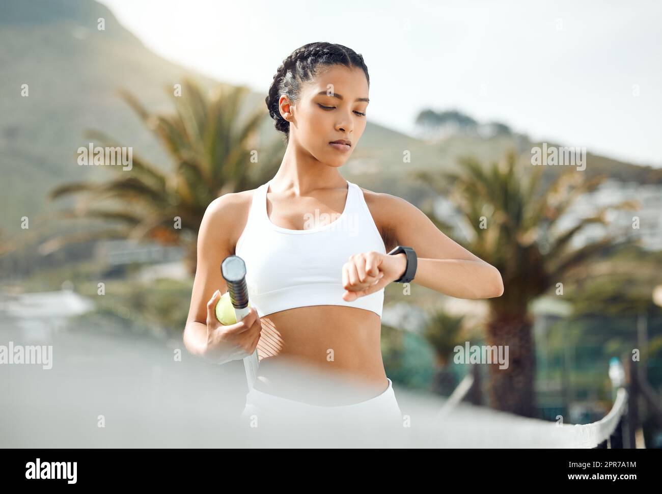 My opponent should be here any minute now. a sporty young woman checking the time while playing tennis outdoors. Stock Photo