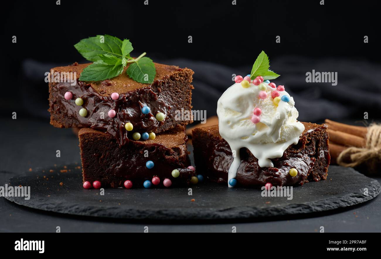 Baked pieces of chocolate brownie pie on a black table, on top of a scoop of ice cream Stock Photo