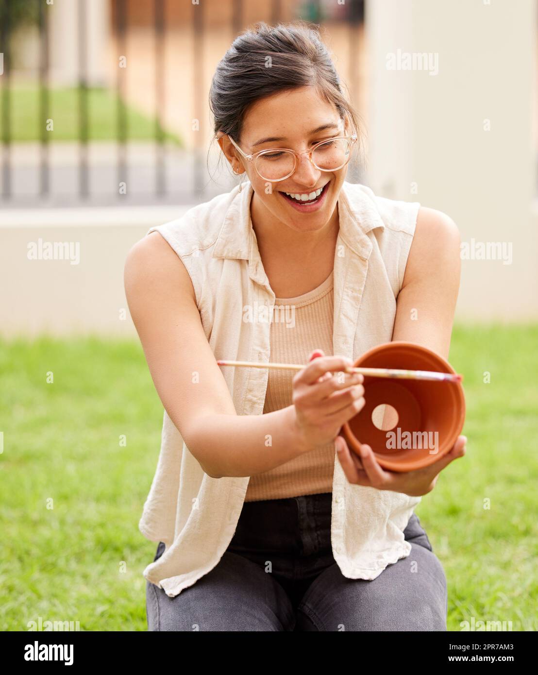 Almost all creativity requires purposeful play. s young woman painting a pot in the garden at home. Stock Photo