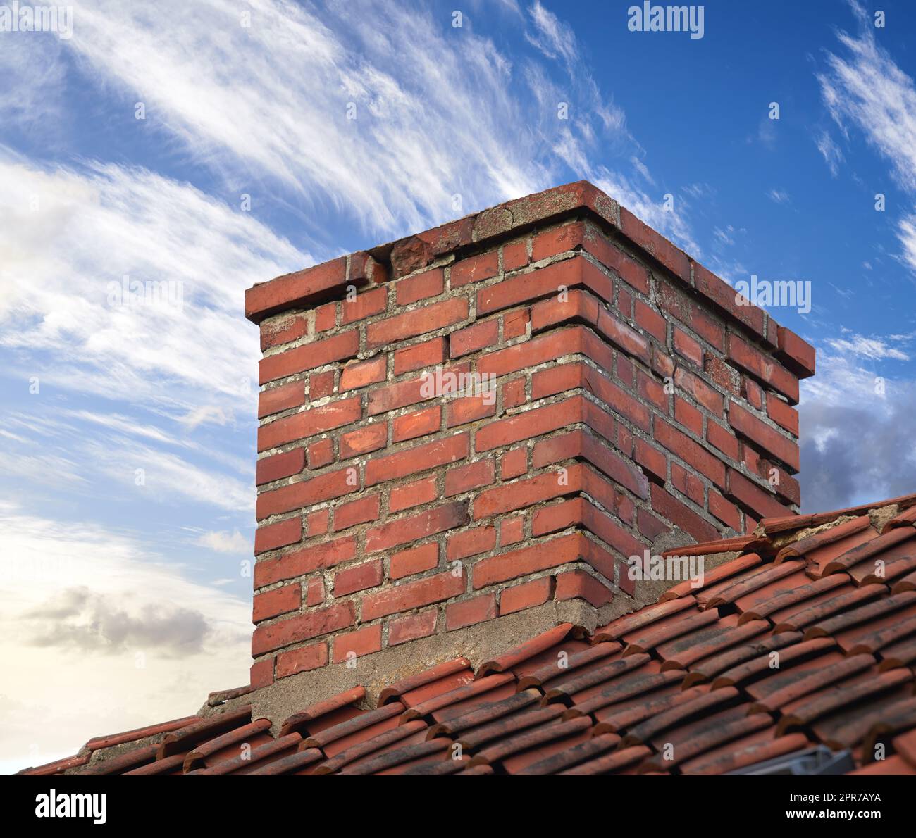 Closeup of red brick chimney chute against blue sky with clouds for combustion gas or home insulation on tiled roof. Architecture design on house building for smoke extraction from fireplace furnace Stock Photo
