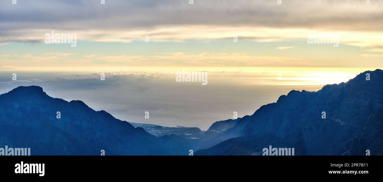 Beautiful landscape of a mountain during sunset with a cloudy sky on a summer day. Peaceful and scenic view of peaks during a golden sunrise with copy space. Aerial view of uncultivated nature Stock Photo