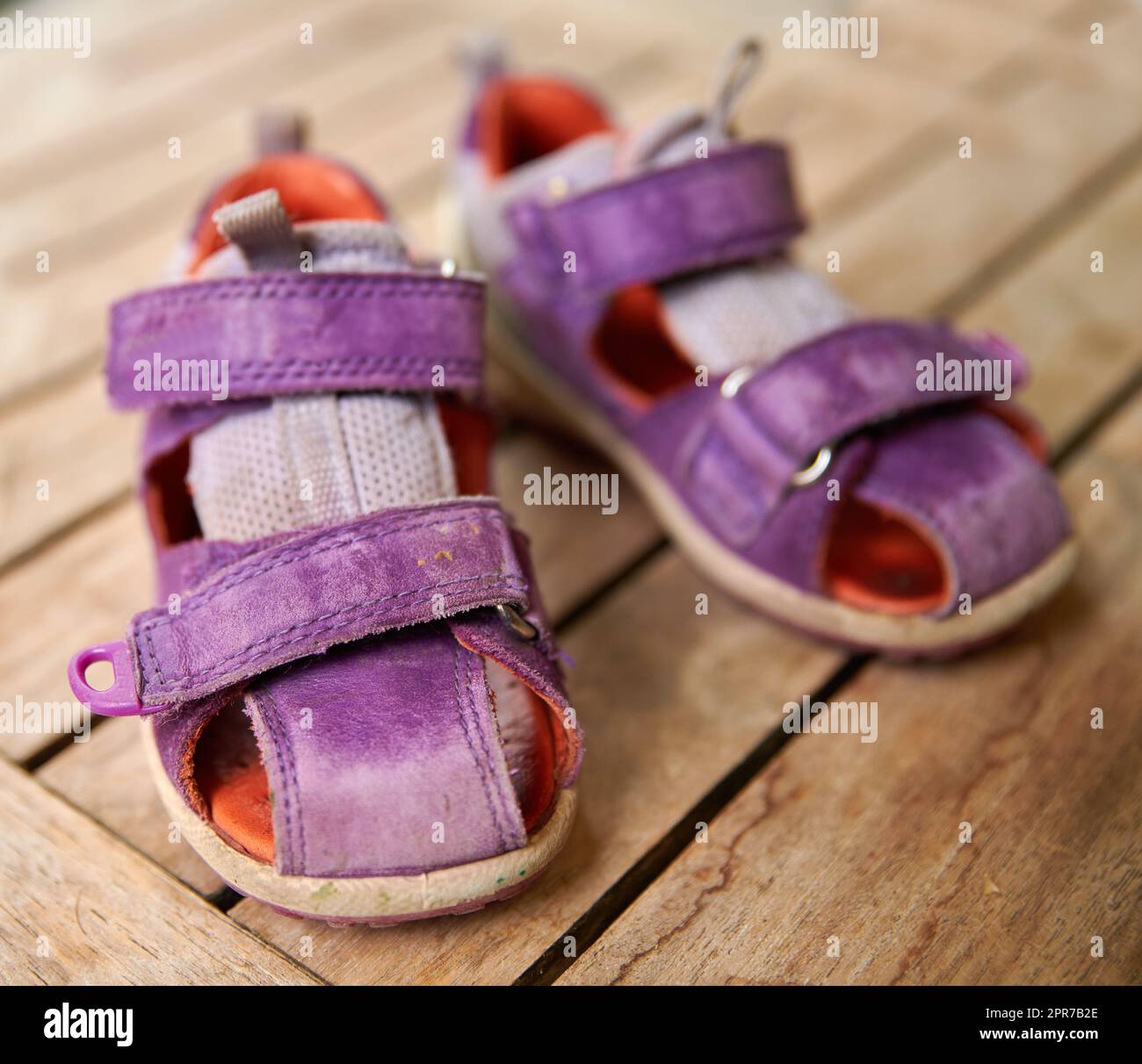 Top view of purple baby shoes on a table at home from above. Little girl footwear symbolizing new life, beginnings and pregnancy. Small stylish and fashionable sandals of a playful child on a desk Stock Photo