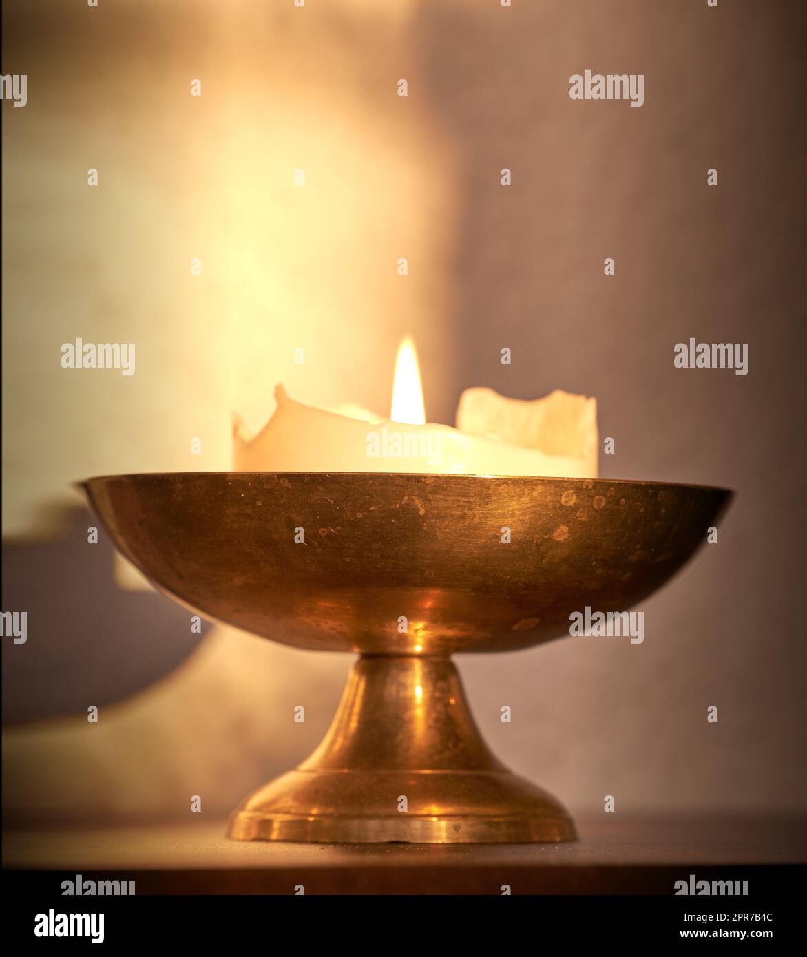Lit candle on a table at home for warmth and brightness. Beautiful house decoration used for aroma, good scent and to bring light to a room. Candles represent light, illumination, and purification Stock Photo