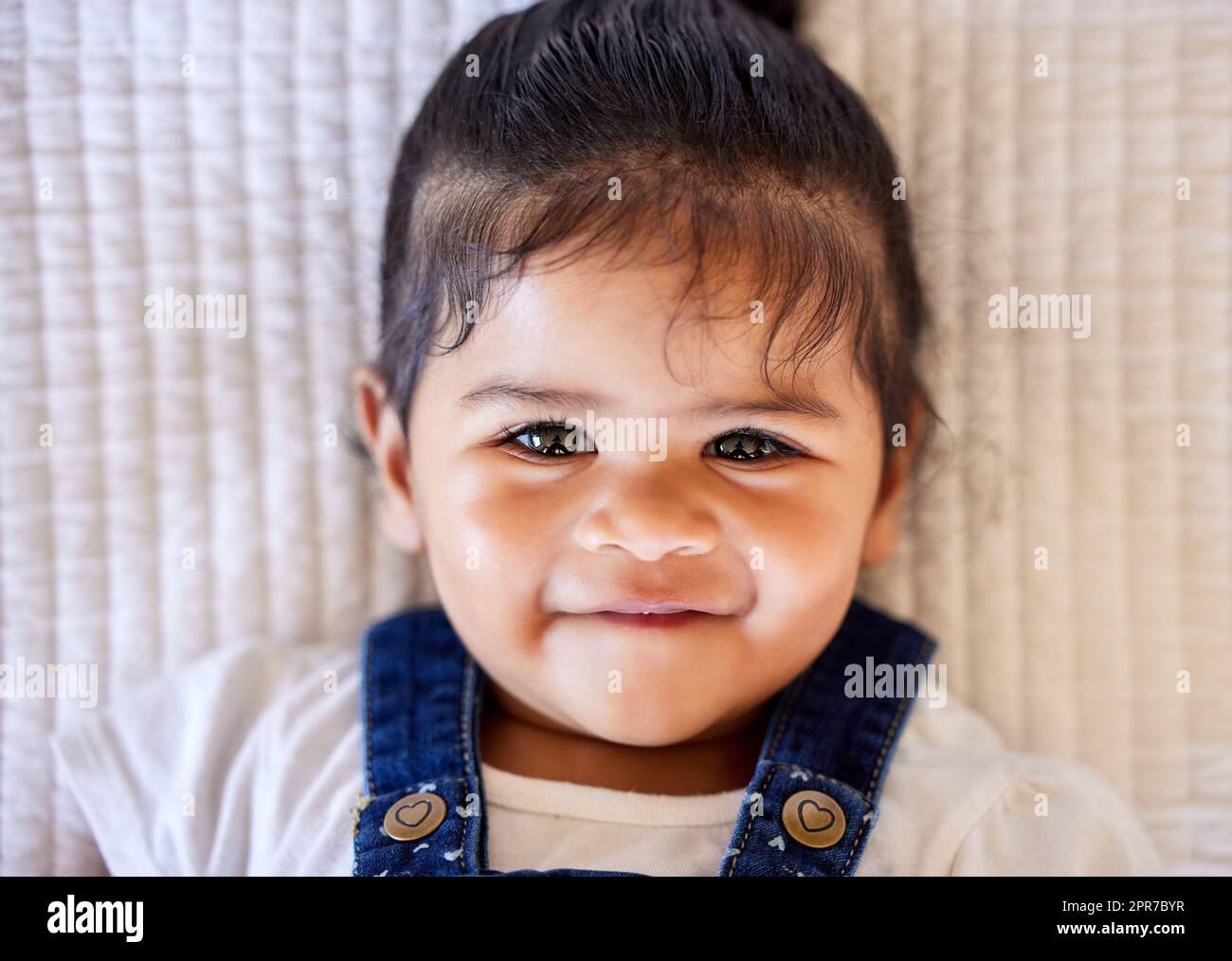 Face of adorable baby smiling at camera. Portrait of an adorable little baby girl lying on bed and looking cheerful Stock Photo