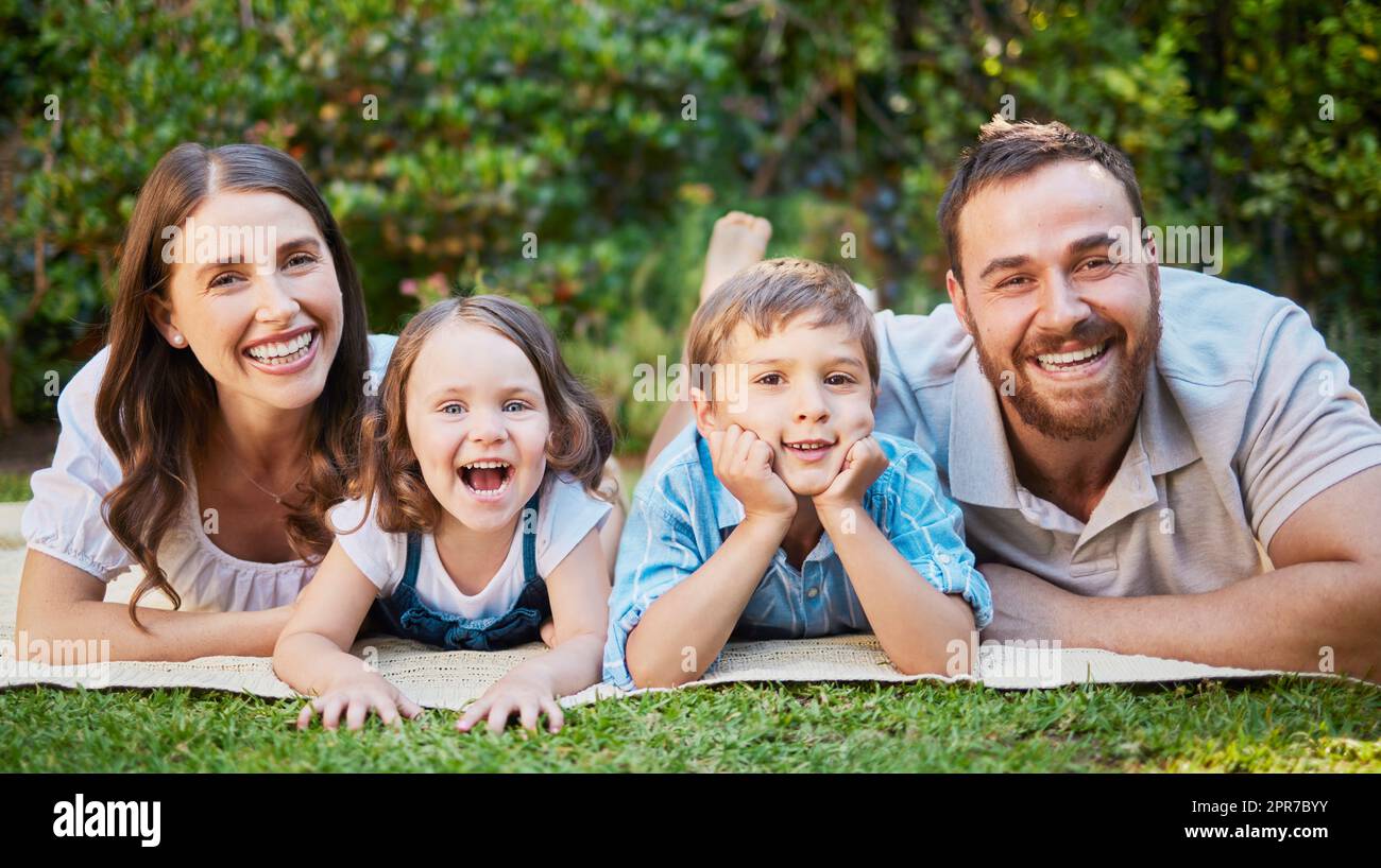 Portrait of cheerful caucasian family on a picnic lying on the lawn together. Happy couple with their two children spending time in nature. Little boy and girl having fun outside with parents Stock Photo