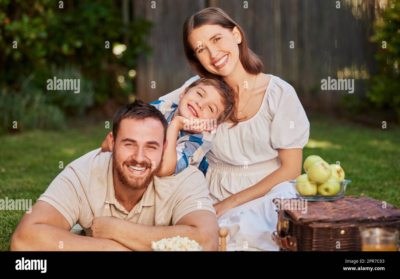 A happy family with a child having a picnic in the garden. Portrait of a smiling, cute little boy with his parents relaxing in the backyard. A mother and father having fun with their son on the grass Stock Photo