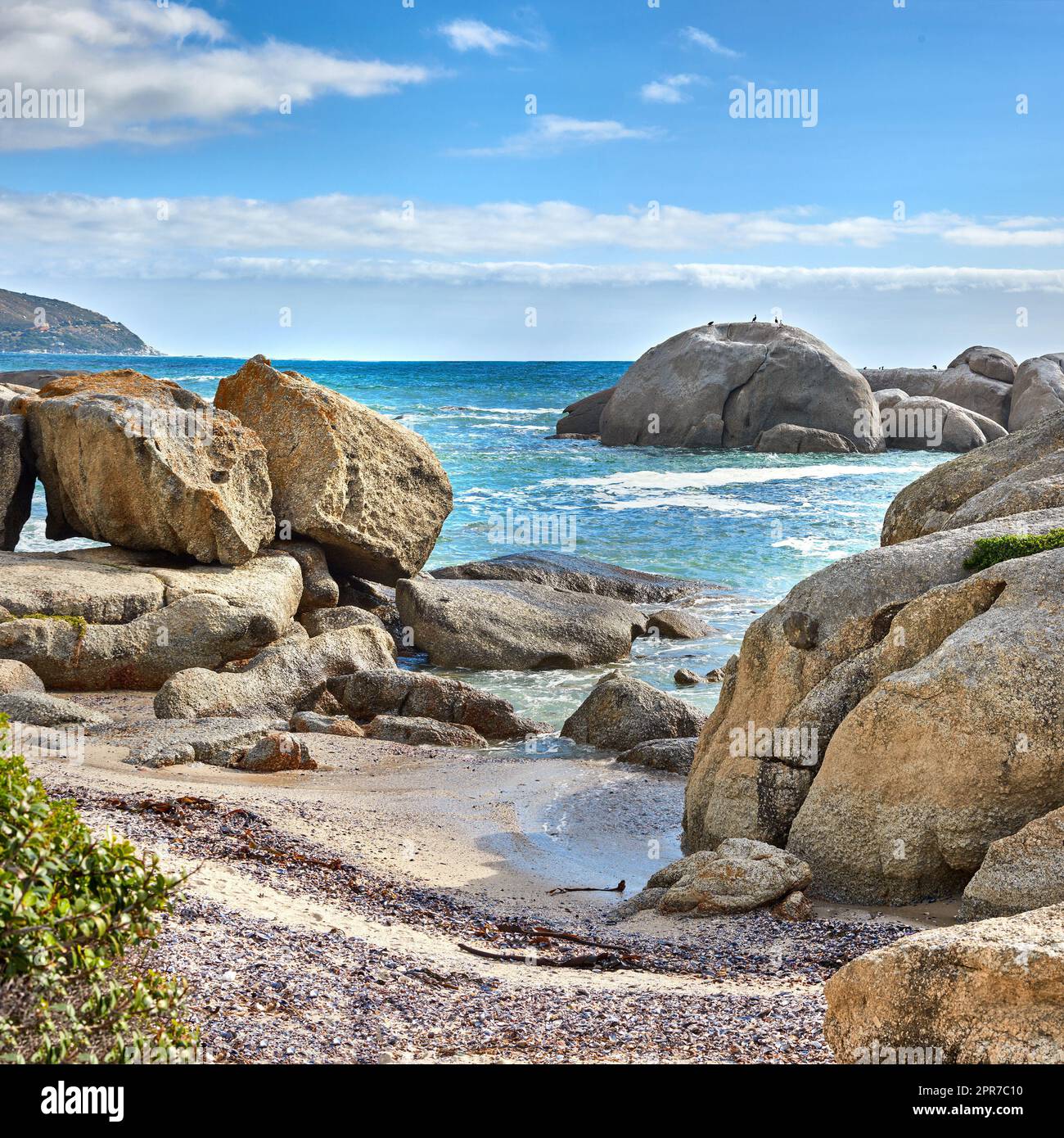 Landscape of beautiful large boulders in the ocean with a blue cloudy sky. Rock or granite structures shining under the sun near calm foamy waves at a popular beach location, Cape Town, South Africa Stock Photo