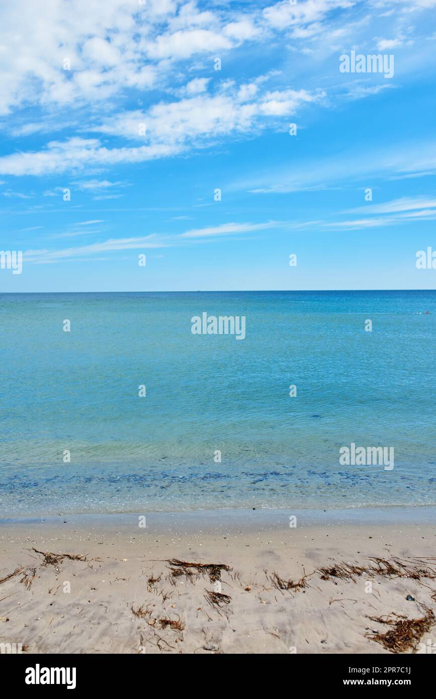 Copy space at the sea with a blue sky background. Calm ocean waves at an empty beach. The scenic landscape for a relaxing summer holiday. Cloudy sky and clean water at the seashore. Stock Photo