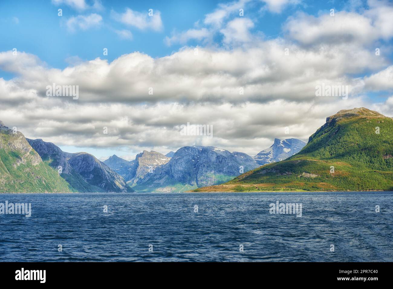 Landscape of mountains north of polar and arctic circle in Bodo, Norway. Scenic view of green hills surrounded by ocean in remote area with clouds. Traveling abroad, overseas for holiday and vacation Stock Photo