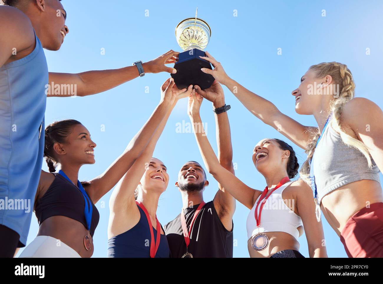 A diverse team of athletes celebrating a victory with a golden trophy and looking excited. A fit and happy team of professional athletes rejoicing after winning an award at an athletic sports event Stock Photo