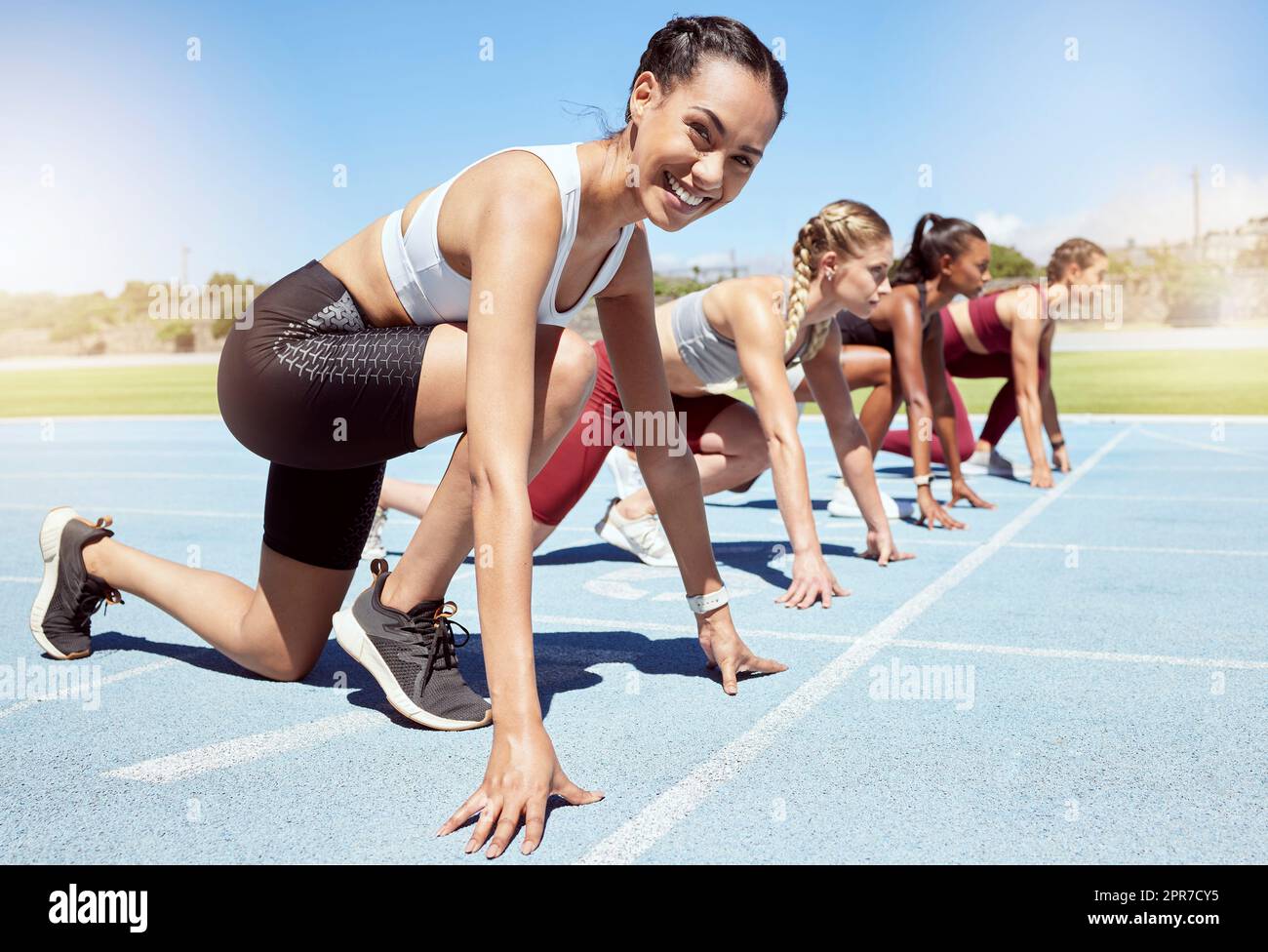 Portrait of female athlete motivated and ready to compete in track and field olympic event. Diverse group of competitive women with hands on the starting line ready to race and determined to win Stock Photo