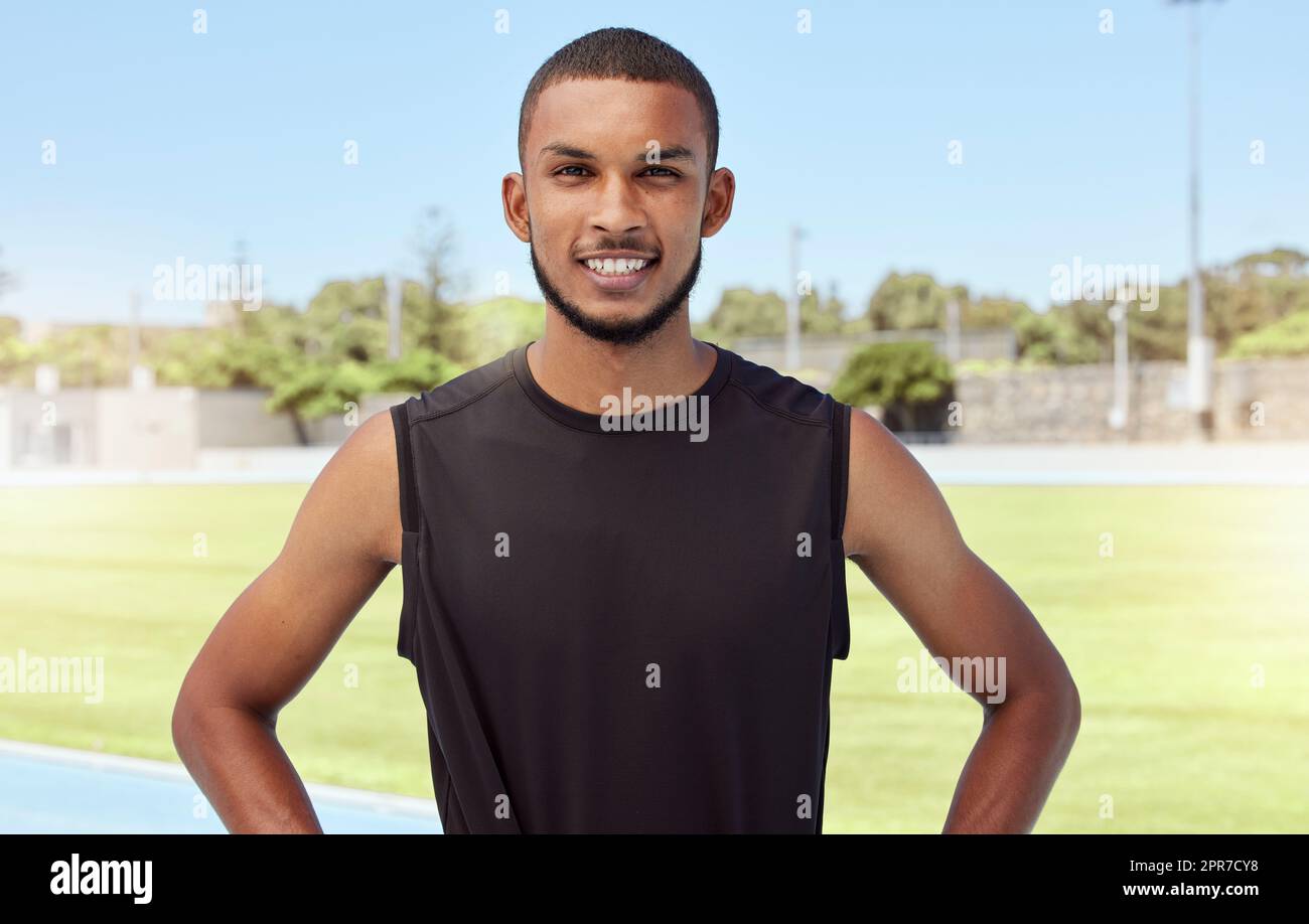 Portrait of a fit active young athlete standing alone before going for a run on a track field. Latino male looking confident and smiling outside getting ready to do his daily routine exercise outside Stock Photo