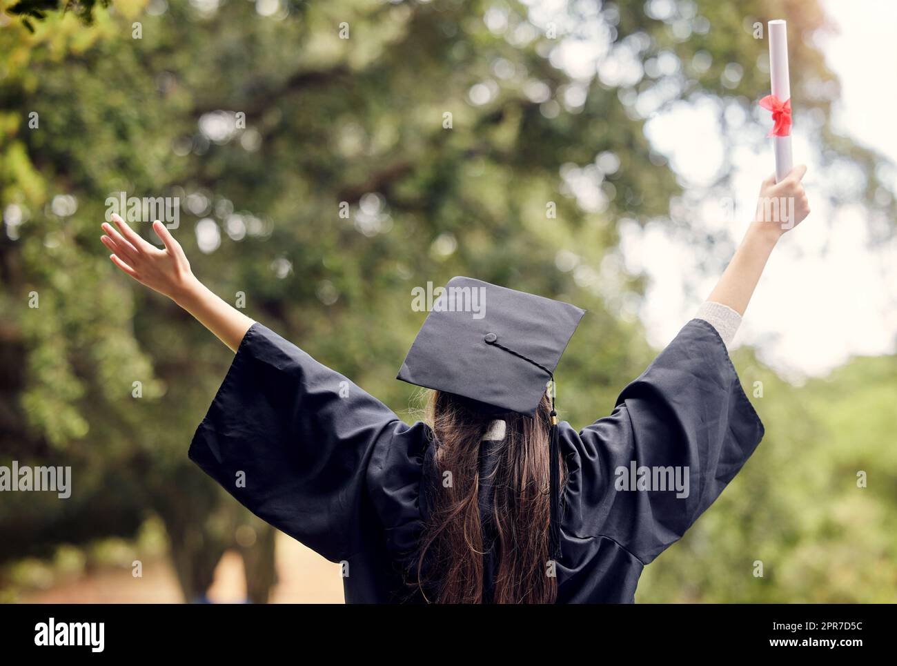On the path to success and happiness. Rearview shot of a young woman cheering on graduation day. Stock Photo
