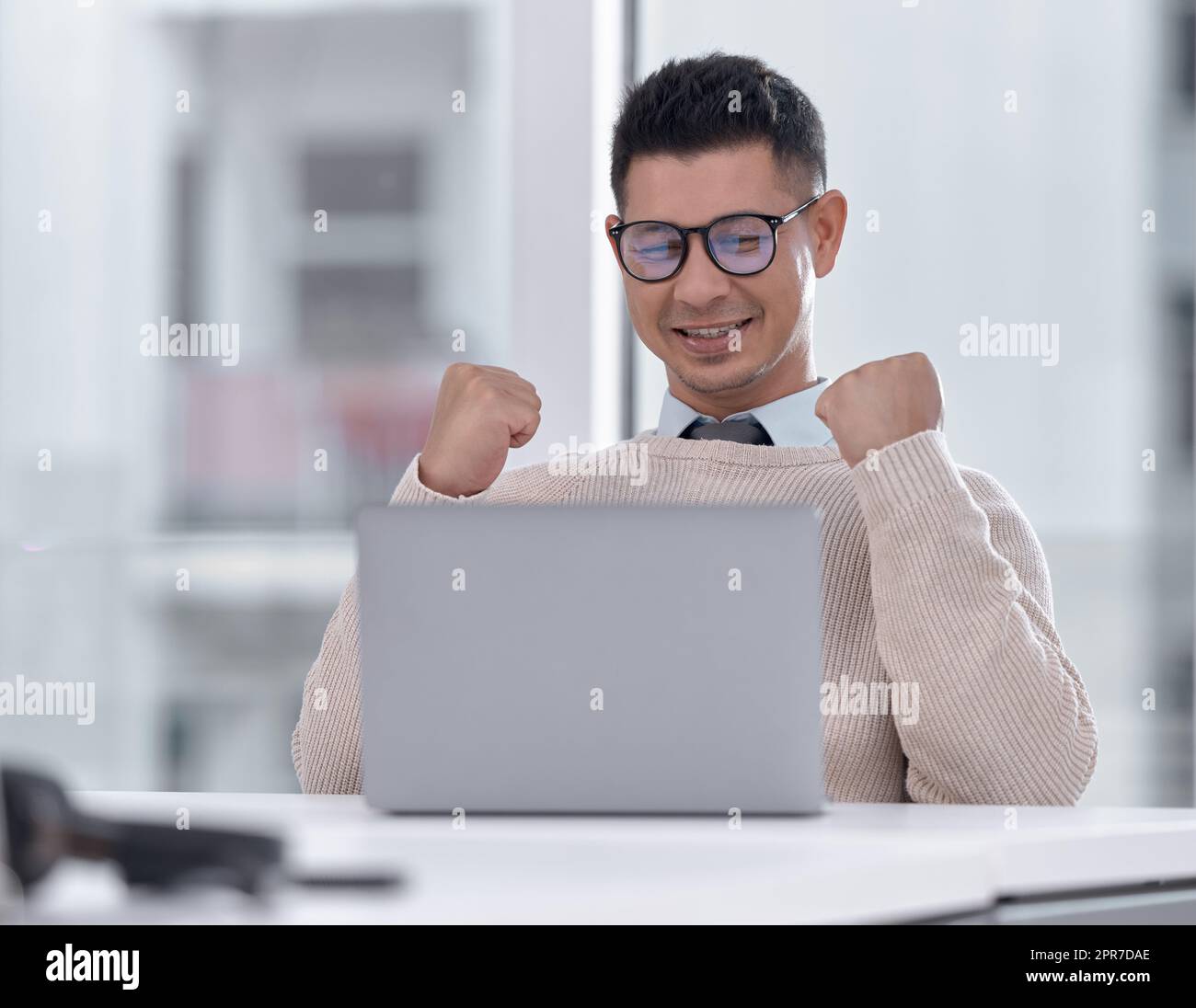 Hes just been presented with an amazing offer. a young businessman cheering while working on a laptop in an office. Stock Photo