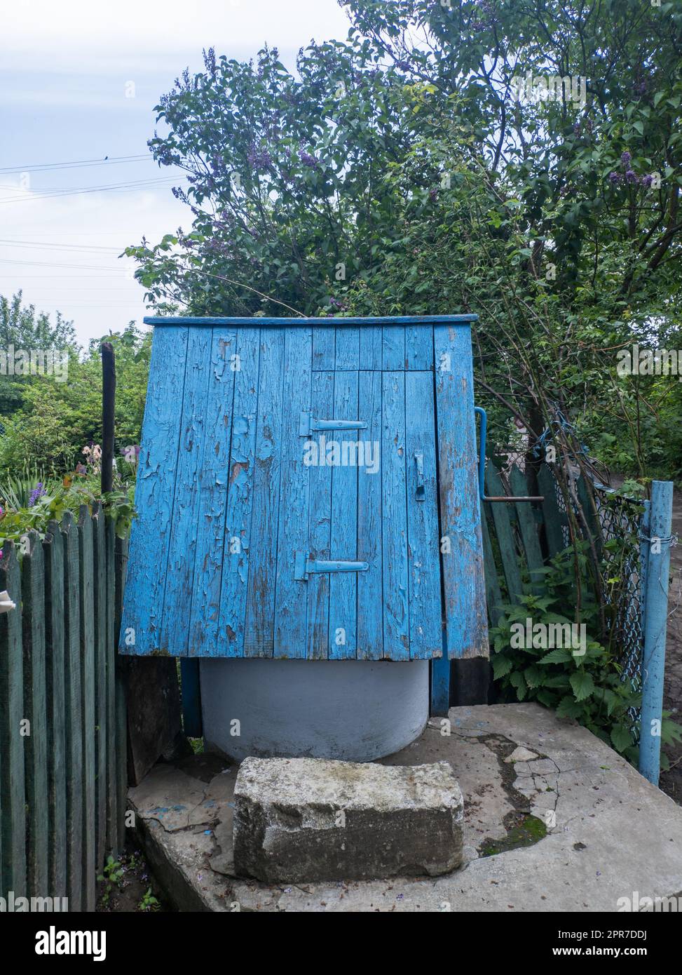 Ancient artesian well and wooden roof with hanging wood bucket in the village among the trees. Stock Photo