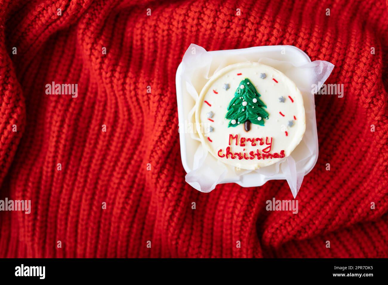 Christmas cake with the inscription merry christmas, decorated with icing, on a red background, top view. Stock Photo