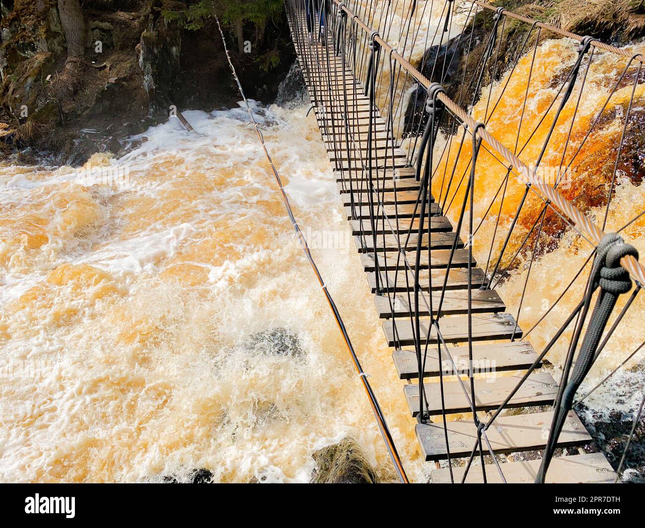 Above the fountain with yellow-brown water and protruding stones there is a rope wooden ladder Stock Photo