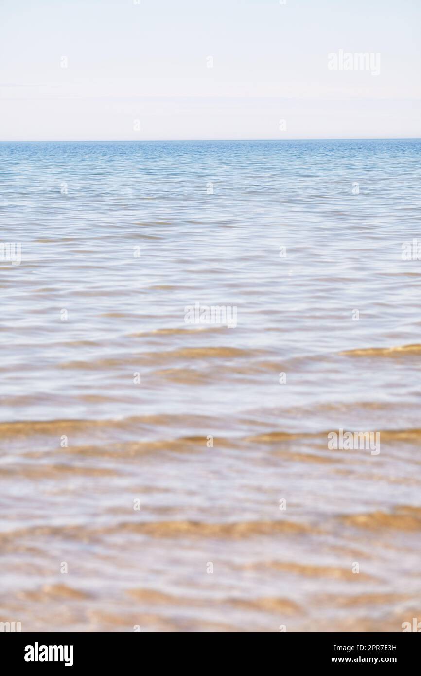 Copy space at the sea with a clear blue sky background above the horizon. Calm ocean waters at an empty beach. Peaceful and scenic coastal landscape for a relaxing and zen summer getaway in nature Stock Photo
