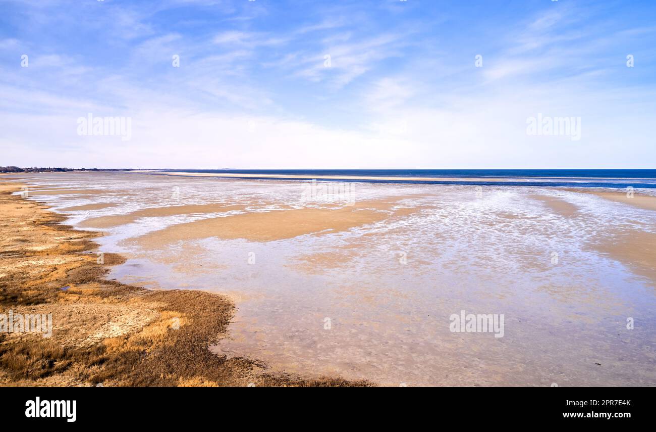 Landscape of beach sand with ocean and blue cloudy sky background on the Eastcoast shoreline line Kattegat, Jutland, near Mariager fjord, Denmark. Scenic view of sea water on sand during the tide Stock Photo