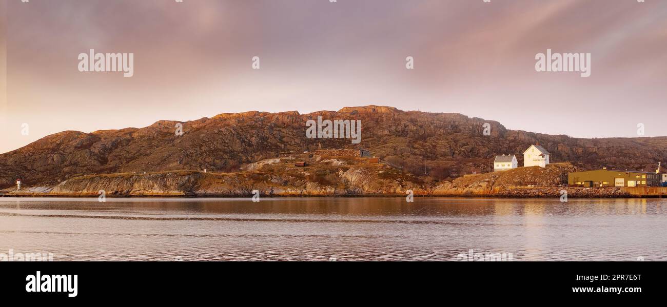 Sea landscape near a mountain with houses on a hill. The ocean or a large lake with residential buildings in the distance outdoors during sunset on a cloudy day. Perfect location for summer vacation Stock Photo