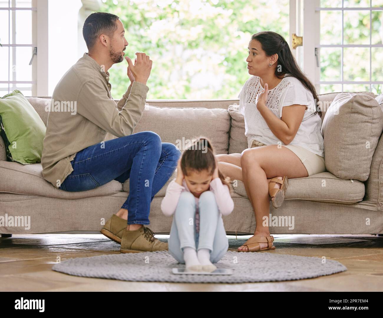 She cant listen any longer. Shot of a little girl covering her ears while her parents argue at home. Stock Photo