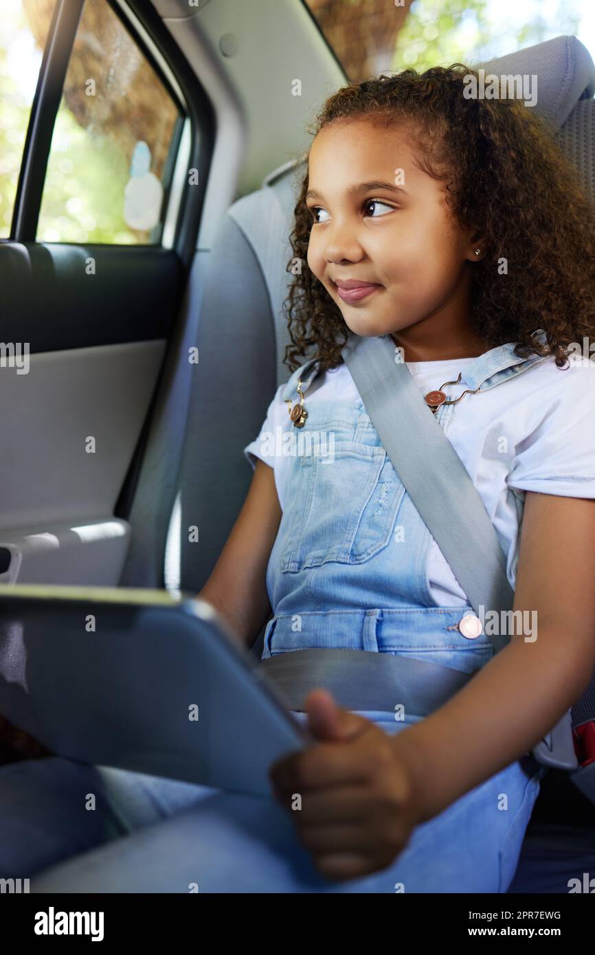 Shes got everything she needs for the trip. Cropped shot of an adorable little girl using her tablet while sitting in the backseat of a car. Stock Photo