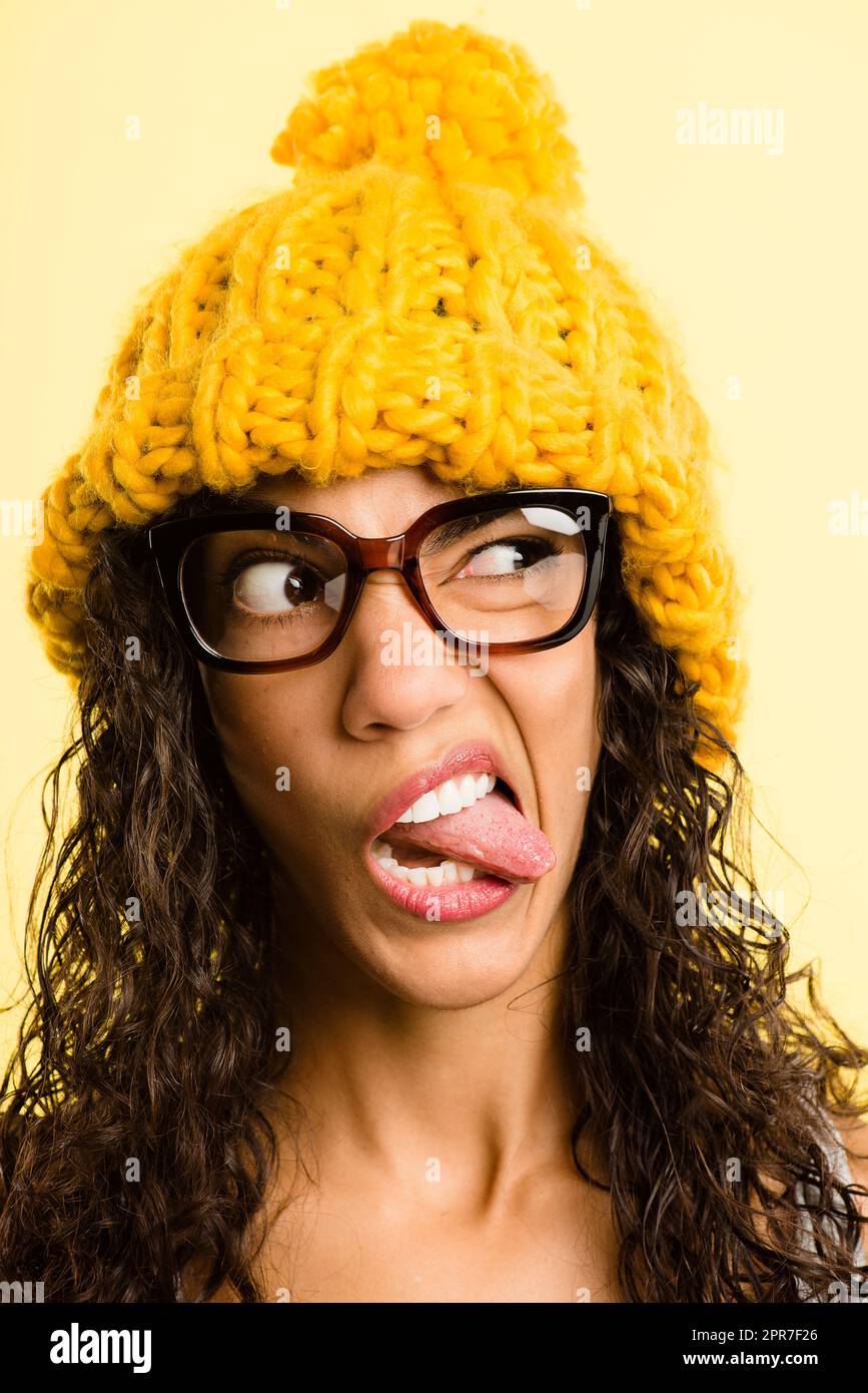 Yellow is such a playful colour. Shot of an attractive young woman standing alone in the studio and pulling funny faces while wearing a beanie. Stock Photo