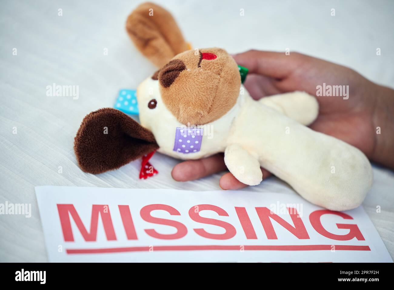 One missing child is one too many. Closeup shot of an unrecognisable woman holding a teddy bear alongside a missing person poster. Stock Photo