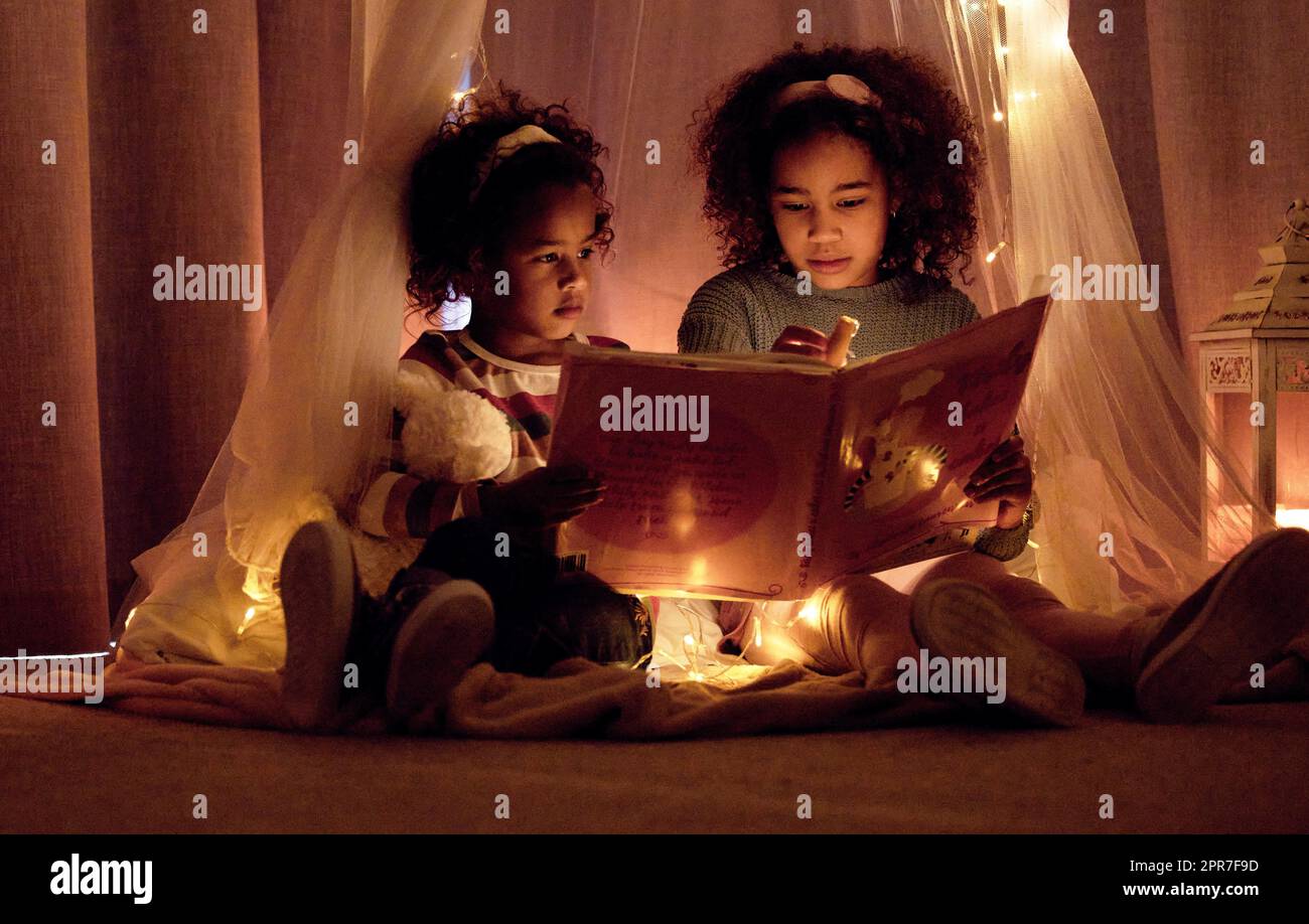 A book is a gift you can open again and again. Shot of two adorable little girls reading a book together in a room at night. Stock Photo